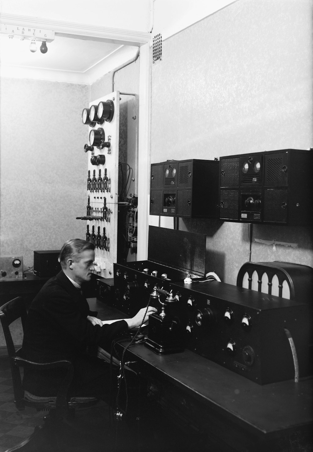 Mężczyzna w garniturze obsługuje zabytkowy sprzęt komunikacyjny przy biurku.
