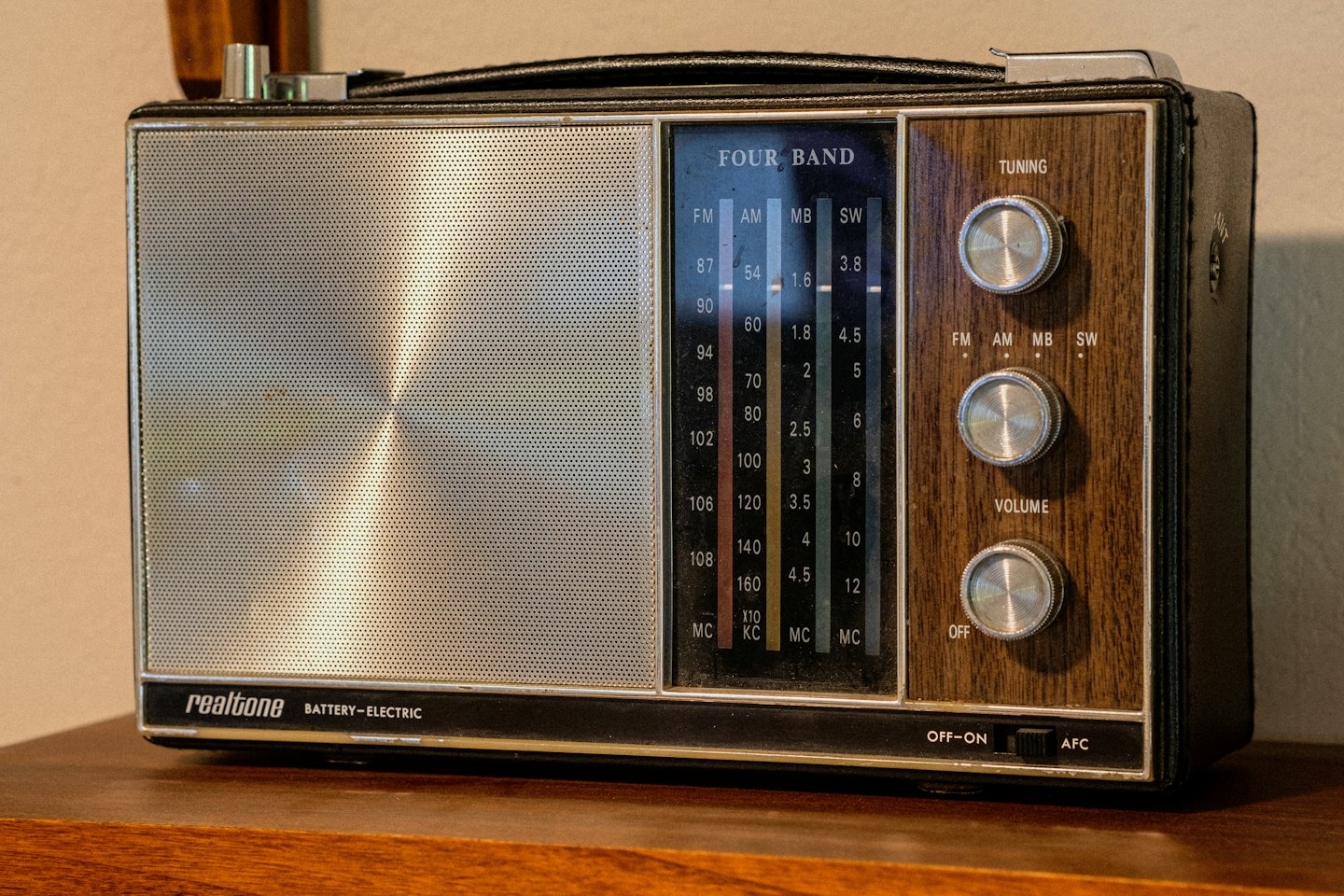 Przenośne radio Reotone w stylu vintage z srebrną maskownicą głośnika i drewnianymi pokrętłami.