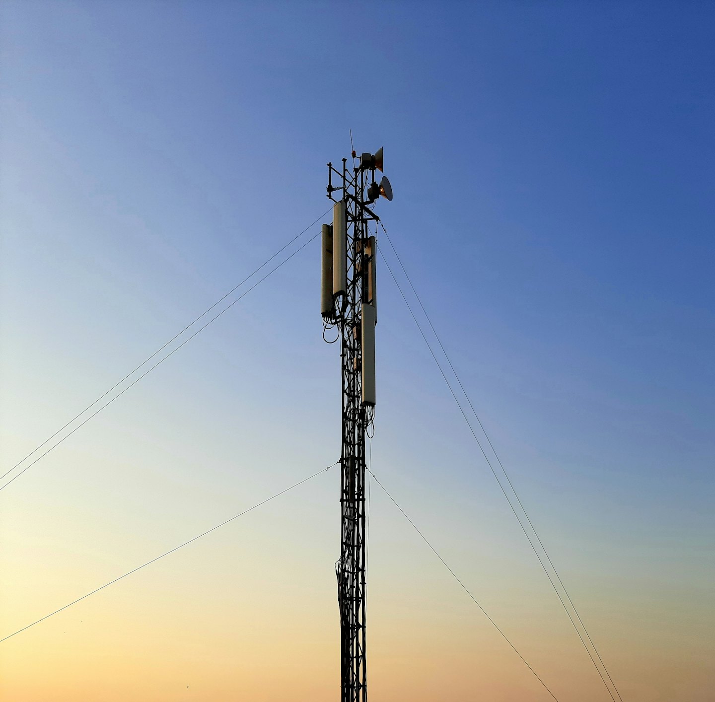 Wieża telekomunikacyjna z antenami na tle nieba o zachodzie słońca.